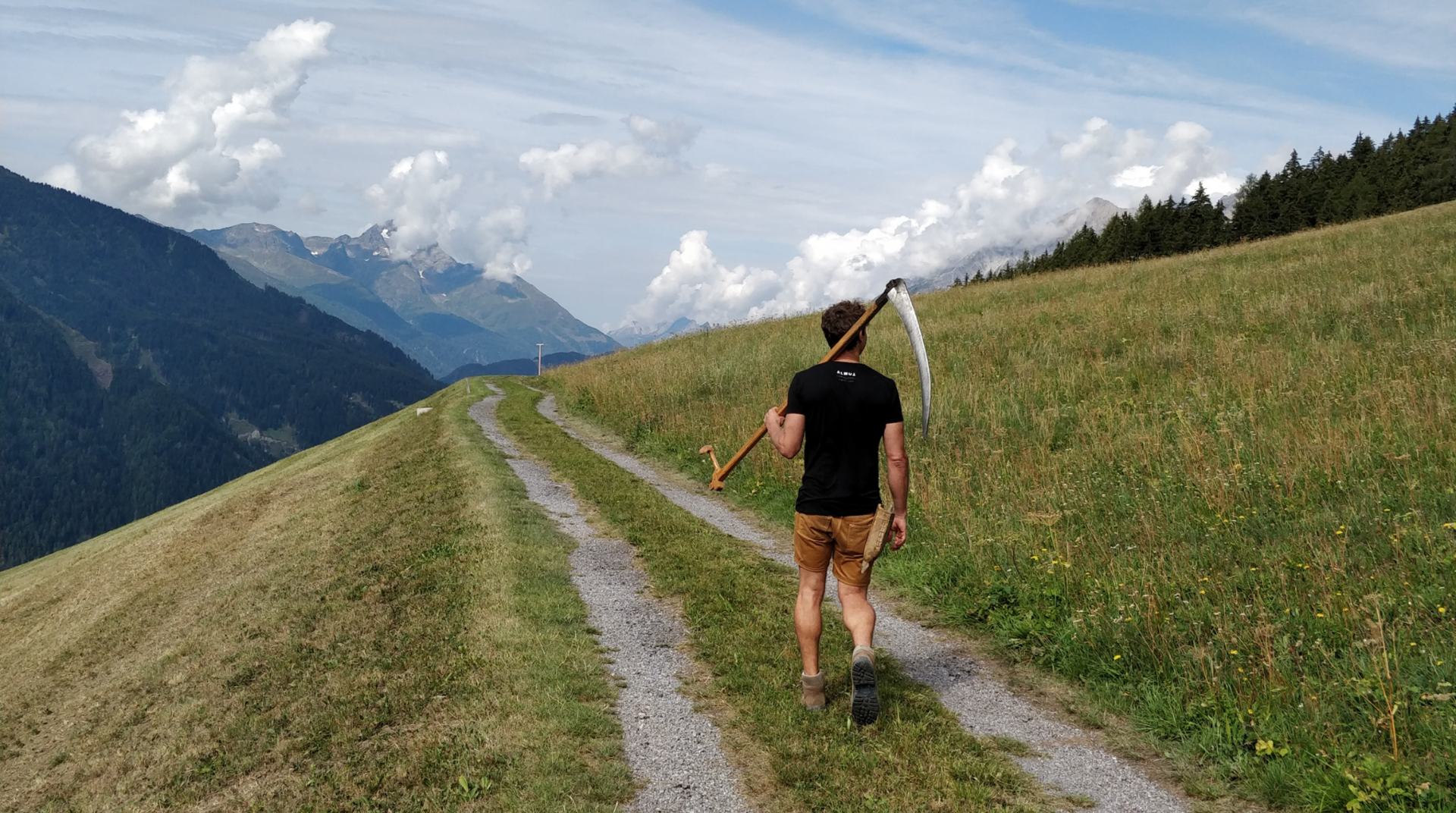 Herr mit Sense geht in einem Traumhaften Alpenpanorama spazieren. Hier in Tirol kommt das Almheu für die Lampen her.