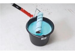 Fliesendispersionsgrund CERAfix 101, blaue Farbe im schwarzen Eimer, Malerrolle beim Hineintauchen in die Farbe