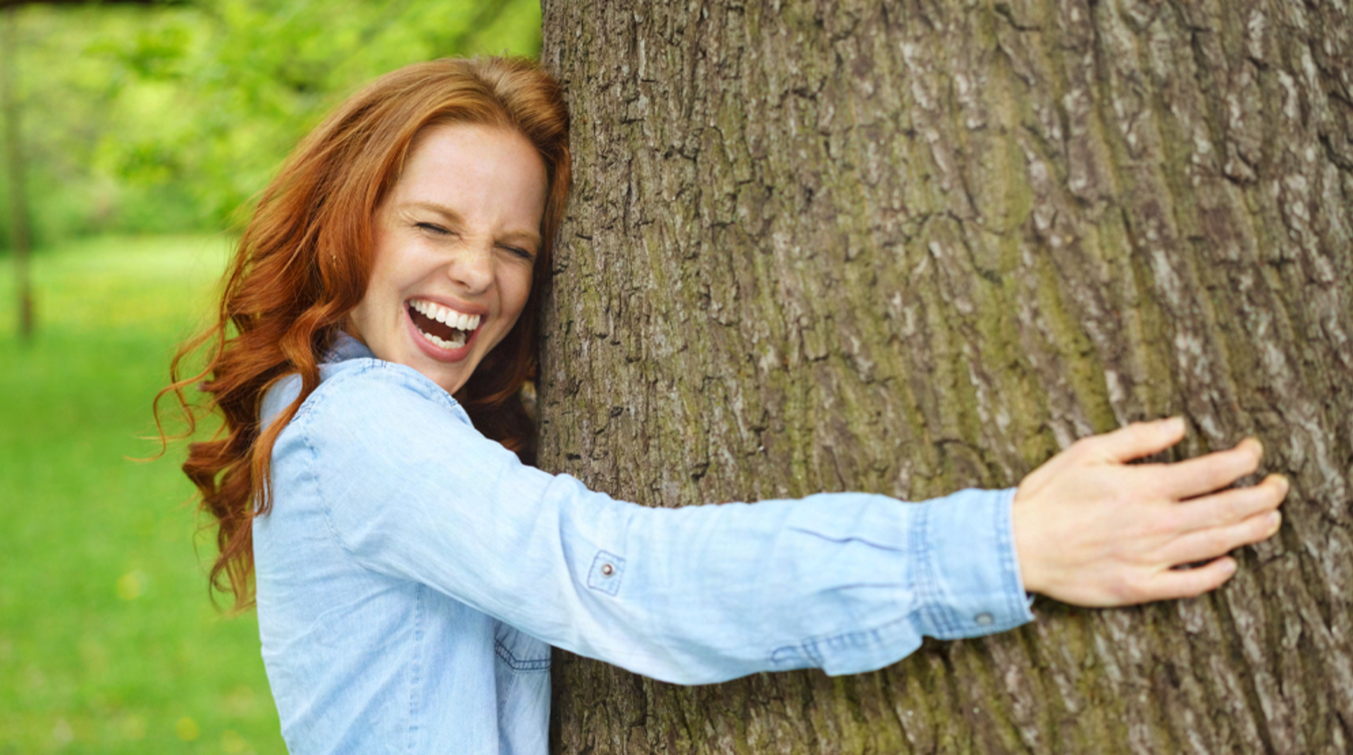 Rothaarige junge Frau umarmt Baum