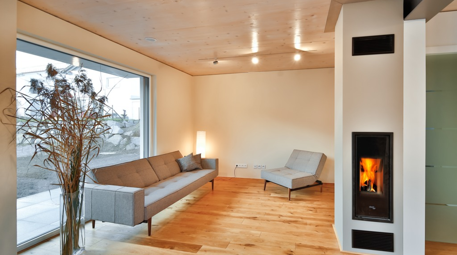 Modernes weißes Wohnzimmer mit Couch, Sessel, Pflanze und Holzofen