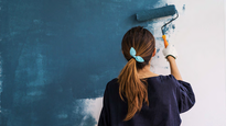 Junge Frau streicht eine Wand blau