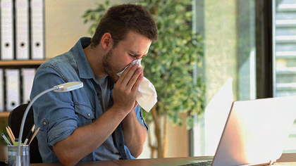 Mann mit einer Allergie niest in ein Taschentuch